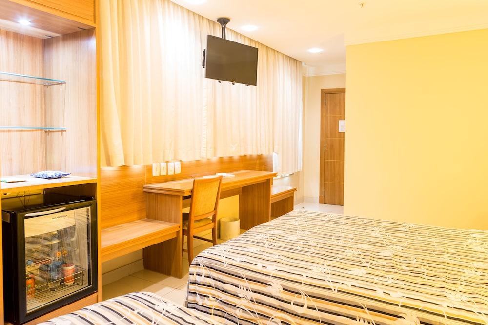 Hotel Atlantico Business Centro Rio de Janeiro Exterior foto The photo shows a hotel room with two beds featuring striped bedding. There is a wooden desk and chair near a window with light-colored curtains. A flat-screen television is mounted on the wall, and there appears to be a small refrigerator or mini-ba