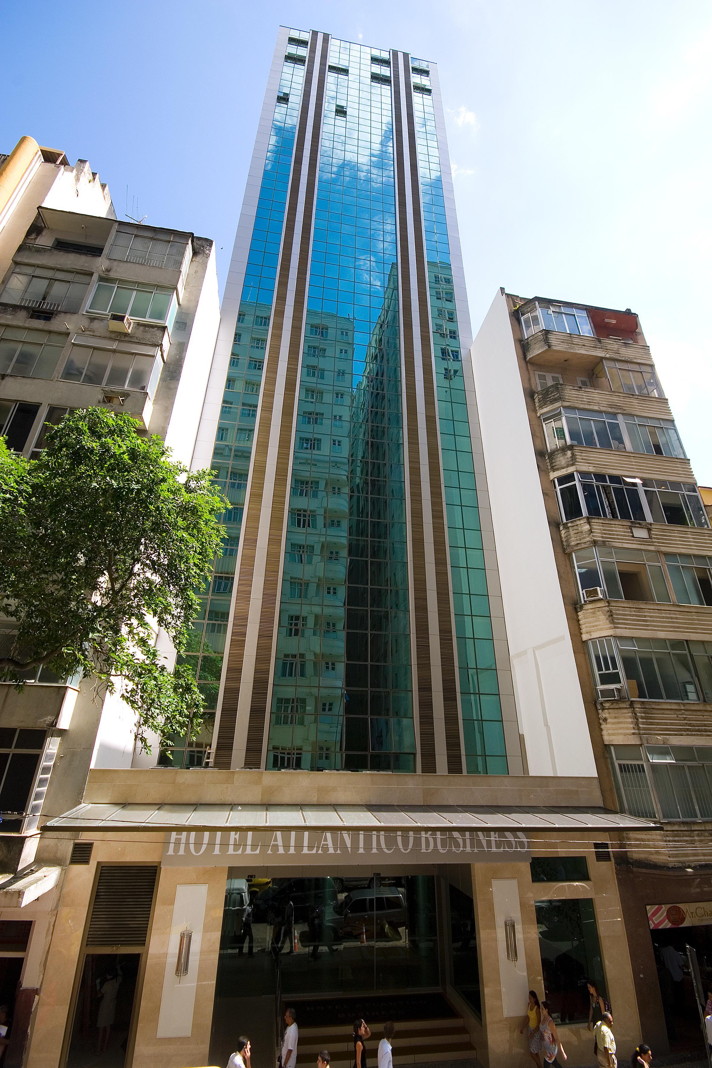 Hotel Atlantico Business Centro Rio de Janeiro Exterior foto The photo shows a modern multi-story building with a sleek glass facade. The building appears to have several floors with large windows, reflecting sunlight, and is flanked by a tree on one side and an older, more traditional residential structure on
